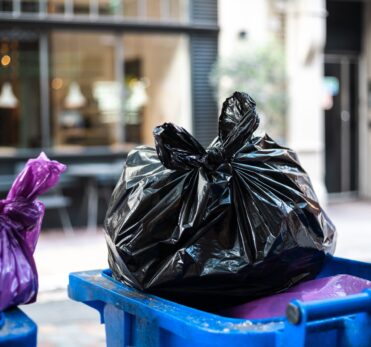 Purple and black bags of trash on a garbage bin during daytime