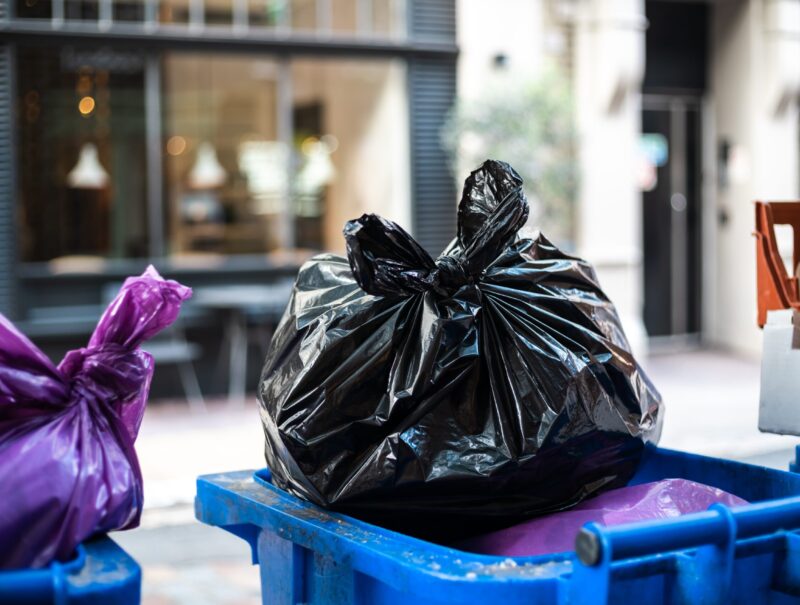 Purple and black bags of trash on a garbage bin during daytime